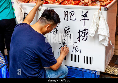 Ein Mann schreibt ein Zeichen in der chinesischen Außen ein Lebensmittelgeschäft, Bowrington Straße Food Market, Hongkong, China Stockfoto