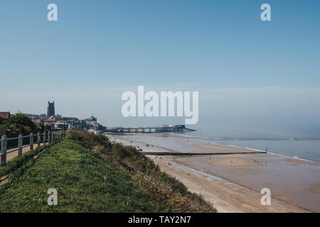 Cromer, Großbritannien - 20 April, 2019: die Menschen gehen auf einem küstenweg neben dem Strand in Cromer, Stadt und Hafen im Hintergrund. Cromer ist eine Küstenstadt i Stockfoto