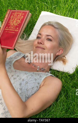 Ein modernes, blond, Frau, lesen Sie ein Buch in einem Park im Sommer, sitzend auf grünem Gras, stehend Festlegung auf Gras Stockfoto