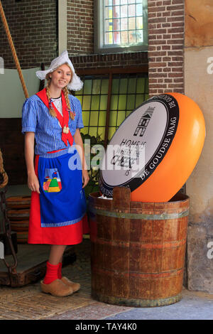 Blonde teen in traditionellen niederländischen Kleidung mit der Holzschuhe und einem riesigen ganze Käse in Gouda (Niederlande), Süd Niederlande Süß Stockfoto