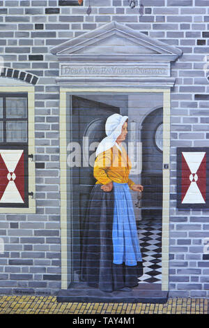 Eine Dame in einem traditionellen Kleid am Eingang ihres Hauses auf einer Graffiti/Wandmalerei/Mural in Zierikzee (Zeeland), Niederlande Stockfoto