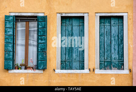 Foto von drei verwitterte, grüne Windows gegen eine texturierte gelb Putz an der Wand in der mittelalterlichen Wasser Stadt Venedig, Italien gemalt. Stockfoto