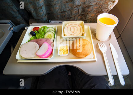 Mahlzeit per Flugzeug service Fach für Economy Class, Fleisch, Obst, Salat, Gurke, ein Glas Saft und Butter. Messer und Gabel aus Kunststoff für Sicherheit. Stockfoto