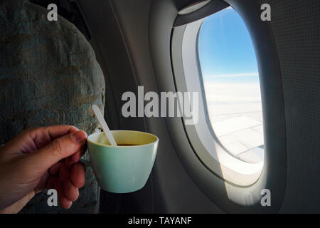 Blick auf eine Tasse Kaffee von mans hand Vor ein Flugzeug Fenster In-flight auf Flugzeuge. Stockfoto