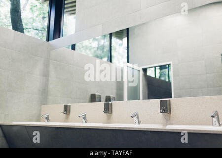 Moderne Innenausstattung in der öffentlichen Toilette. Neue Spülen, Armaturen mit Spiegel und Fenster oben. WC Stockfoto