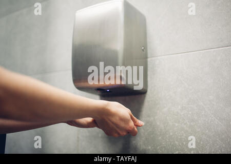 Lufttrockner in der öffentlichen Toilette. Frau Trocknen der Hände im Wasser Schrank. Hygiene Konzept Stockfoto