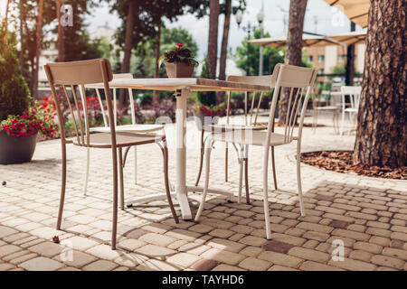 Café im Freien im Sommer. Leere Tische und Stühle mit Bäumen und Blumen, die auf der Straße der Stadt umgeben. Stockfoto