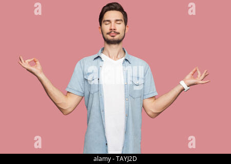 Portrait der Ruhe entspannt gut aussehender bärtiger junger Mann in blau casual style Hemd stehend mit erhobenen Armen und Yoga Meditation ausüben. indoor St Stockfoto