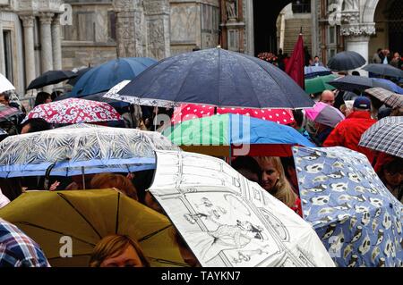 Einen feuchten regnerischen Tag in St. Markusplatz Venedig überfüllt mit Touristen mit bunten Sonnenschirmen, Italien Europa EU Stockfoto
