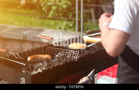 Man kocht Würstchen und Brötchen für Hot Dogs und Burger auf dem Grill im Freien im Sommer Stockfoto