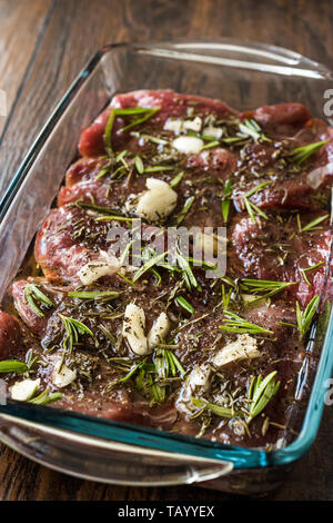 Mariniertes rohes Fleisch Rinderfilet mit Rosmarin, Knoblauch und Olivenöl in Glasschale bereit zu Kochen. Ökologische Lebensmittel. Stockfoto