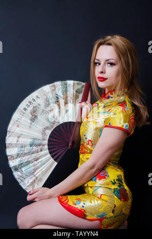 Formschöne Mädchen aus Polen. Junge weibliche Modell im Studio mit schwarzem Hintergrund posiert. Kaukasische Mädchen mit bunten Chinesischen Kleid und Ventilator. Stockfoto