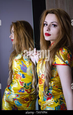 Formschöne Mädchen aus Polen. Junge weibliche model in der Nähe von Spiegel posiert, tragen bunte chinesische Kleid.