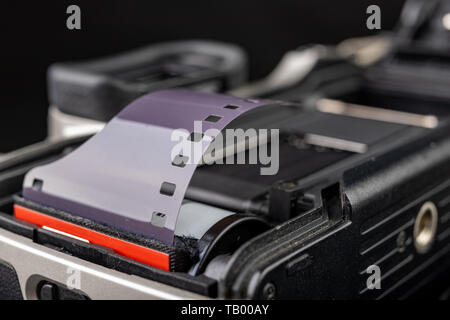 Von alten analogen Kamera und Schwarzen und Weißen neuen Film. Zubehör für die analoge Fotografie auf einen dunklen Tisch. Schwarzen Hintergrund. Stockfoto