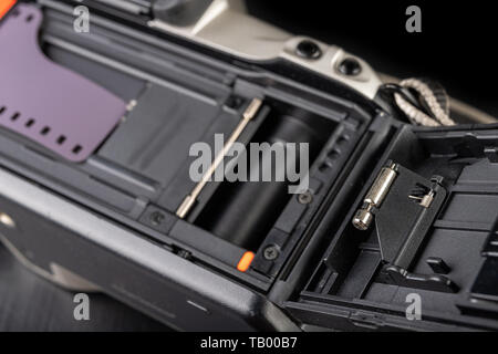 Von alten analogen Kamera und Schwarzen und Weißen neuen Film. Zubehör für die analoge Fotografie auf einen dunklen Tisch. Schwarzen Hintergrund. Stockfoto