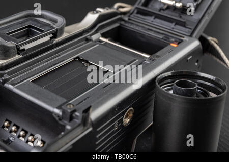 Von alten analogen Kamera und Schwarzen und Weißen neuen Film. Zubehör für die analoge Fotografie auf einen dunklen Tisch. Schwarzen Hintergrund. Stockfoto