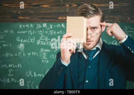 Halten Sie im Verstand. Lehrer formale Abnutzung und Gläser sieht Smart, schwarzes Brett Hintergrund. Bildung Konzept. Mann unrasiert hält Buch vor. Lehrer Stockfoto