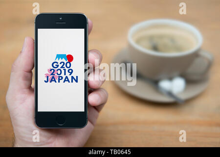 Ein Mann schaut auf seinem iPhone die zeigt die G 20 2019 Osaka Japan Gipfel Logo (nur redaktionelle Nutzung). Stockfoto