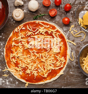 Pizza mit geriebenem Käse und Zutaten rund um Stockfoto