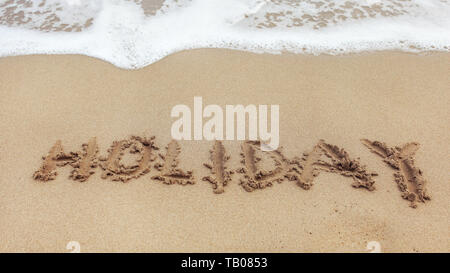 Wort Urlaub auf nassem Sand Strand geschrieben, kleiner Fleck der weißen Meer Wasser im oberen Teil. Stockfoto