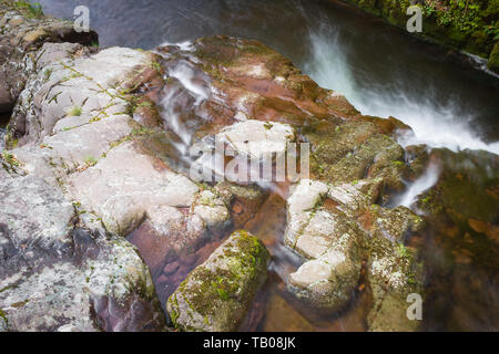 Lange Belichtung Blick von oben auf einem Berg knarren nach unten Kaskadieren des nassen, roten Felsen von Moss Stockfoto