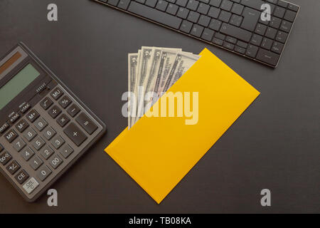 Ein gelber Umschlag mit Geld auf dunklem Leder Schreibtisch, neben einen Rechner und eine Tastatur. Geschäftsidee und hohen Einkommen Erstellung Konzept Stockfoto