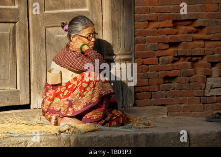 Ältere Frauen (zurück tragen Strebe) sitzen in der Sonne auf Stoop von zu Hause in Altstadt Dhulikhel, Nepal Stockfoto