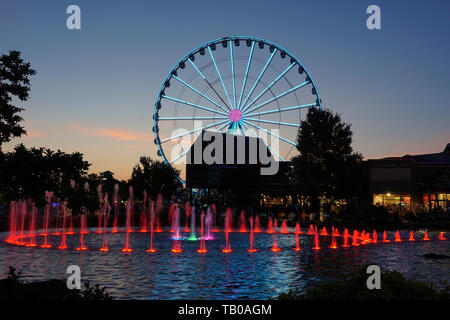 Riesenrad und Springbrunnen mit farbigen Leuchten in der Dämmerung Stockfoto