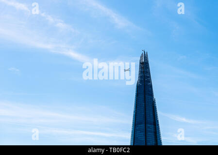 London, UK, 14. Mai 2019: Flugzeug über Shard Gebäude in London fliegen, es sieht so aus, als ob es zum Absturz zu bringen. Low Angle View gegen den blauen Himmel eines sonnigen da Stockfoto