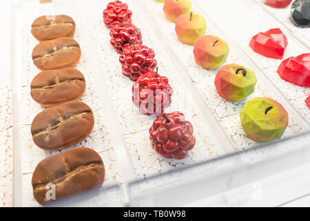 Reihen von bunten Kuchen und Desserts im Schaufenster einer Konditorei. Moderne mousse Dessert süße Snack in Form von Kaffeebohnen, Kirschen Stockfoto