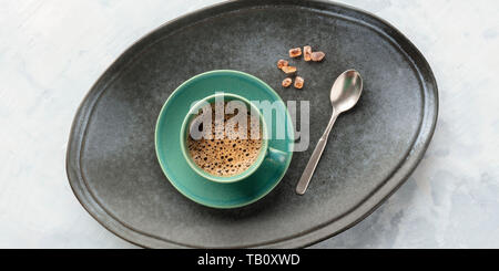 Einen Panoramablick auf eine Tasse schwarzen Kaffee, geschossen von oben auf ein Fach mit karamellisierten Zucker und einem Löffel Stockfoto