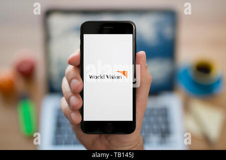 Ein Mann schaut auf seinem iPhone die zeigt die World Vision Logo (nur redaktionelle Nutzung). Stockfoto