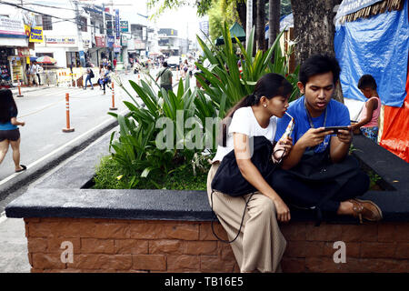 ANTIPOLO CITY, Philippinen - 21. MAI 2019: Ein paar spielt ein Spiel auf einem Smartphone während an einem öffentlichen Park. Stockfoto