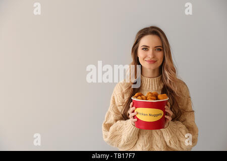 Junge Frau mit Eimer lecker Nuggets auf hellen Hintergrund Stockfoto