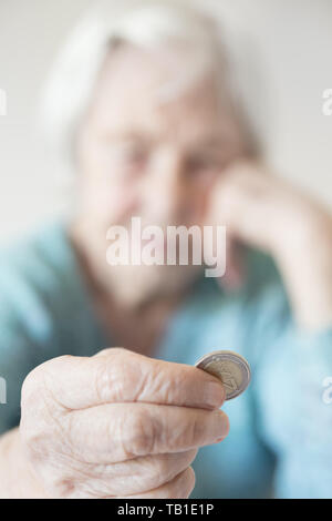 Traurige ältere Frau am Tisch zu Hause sitzt und kläglich, wenn man nur noch die Münze von der Pension in Ihrer Hand. Stockfoto