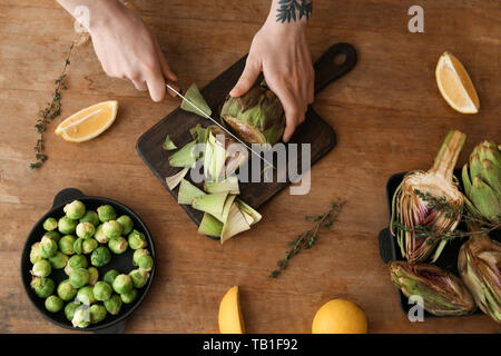 Frau bereitet leckere rohe Artischocken auf hölzernen Tisch Stockfoto
