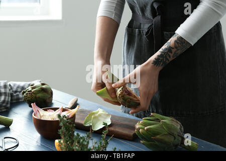 Frau bereitet leckere rohe Artischocken in der Küche Stockfoto