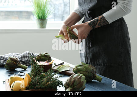 Frau bereitet leckere rohe Artischocken in der Küche Stockfoto