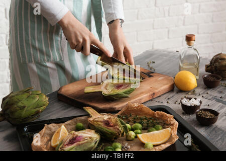 Frau bereitet leckere rohe Artischocken in der Küche Stockfoto