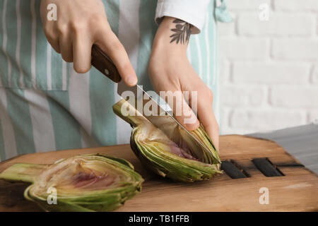 Frau bereitet leckere rohe Artischocken in der Küche Stockfoto