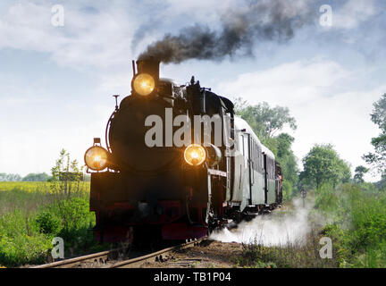 Alte Personenzug auf Spuren durch den Wald. Retro Lokomotive mit einer Dampfmaschine, Rauch und große Lampen. Stockfoto