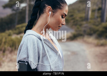 Seitenansicht eines weiblichen Athleten mit Kopfhörer. Frau Musik hören während des Trainings im Freien am Morgen. Stockfoto