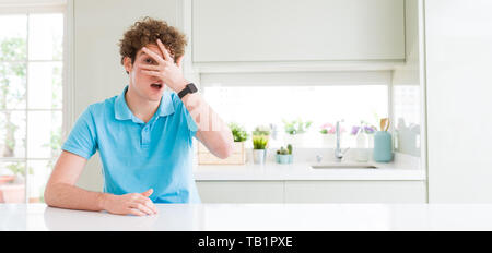 Weite Einstellung junger stattlicher Mann zu Hause peeking im Schock für Gesicht und Augen mit der Hand, schauen durch die Finger mit peinlich Ausdruck. Stockfoto