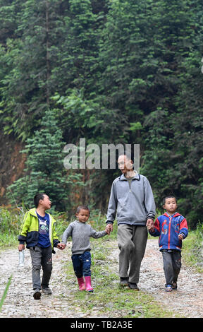 (190530) - Peking, 30. Mai 2019 (Xinhua) - Zhou Hongjun (2. R) führt die Teilnehmer zurück in die Schule nach einer Mittagspause in Rongshui Miao autonomen County, South China Guangxi Zhuang autonomen Region, 28. Mai 2019. Zhou Hongjun, ein Lehrer von 46 Jahren Erfahrung, arbeitet in einer Schule, seit er 16 war in der entlegenen ländlichen Region in Rongshui. Vor 2010 gab es keine Straßenanbindung an die Schule, Alle Schulsachen von Zhou selbst mit einem Buchwert in Pole aufgenommen wurden. Zhou, soll im Jahr 2018 in Rente zu gehen, beschloss, seine Karriere fortsetzen, da es keinen Ersatz Lehrer, seinen Platz einzunehmen. (Xinhua / Lu Boan) Stockfoto