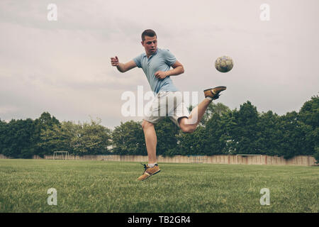 Junger Mann, der seine Fußball-Fähigkeiten kicken den Ball mit seinen hinteren Fuß in einem flachen Winkel auf einem Sportplatz Stockfoto