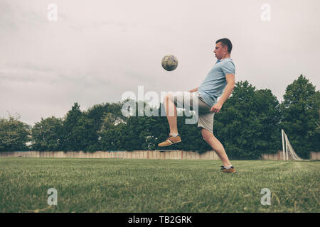 Junger Mann üben ball Steuerung und Koordination prellen einen Ball weg von seinem Fuß während des Trainings auf einem Sportplatz Stockfoto