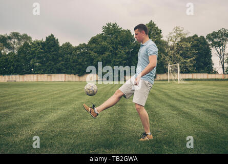 Junger Mann üben ball Steuerung und Koordination prellen einen Ball weg von seinem Fuß während des Trainings auf einem Sportplatz Stockfoto