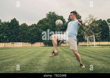 Junge Spieler üben Ballkontrolle mit einem Fußball das Aufprallen auf seinem Oberschenkel während der Ausbildung her einem Spiel oder Wettbewerb auf einem Sportplatz Stockfoto