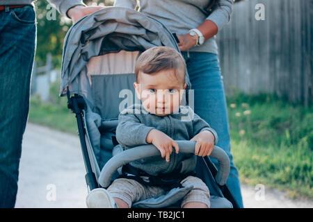 Cute Baby Boy 8-9 Monate sitzen in Buggy mit Papa und Mama zu Fuß auf der Dorfstraße im Freien, Sensibilität für die Natur Konzept Stockfoto