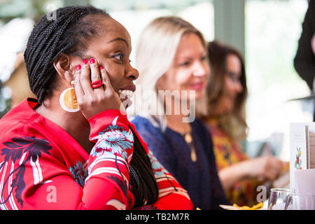 Frau mit cornrows tragen goldene Ohrringe und Red Top an einem Tisch sitzen, aufmerksam zuhören. Stockfoto